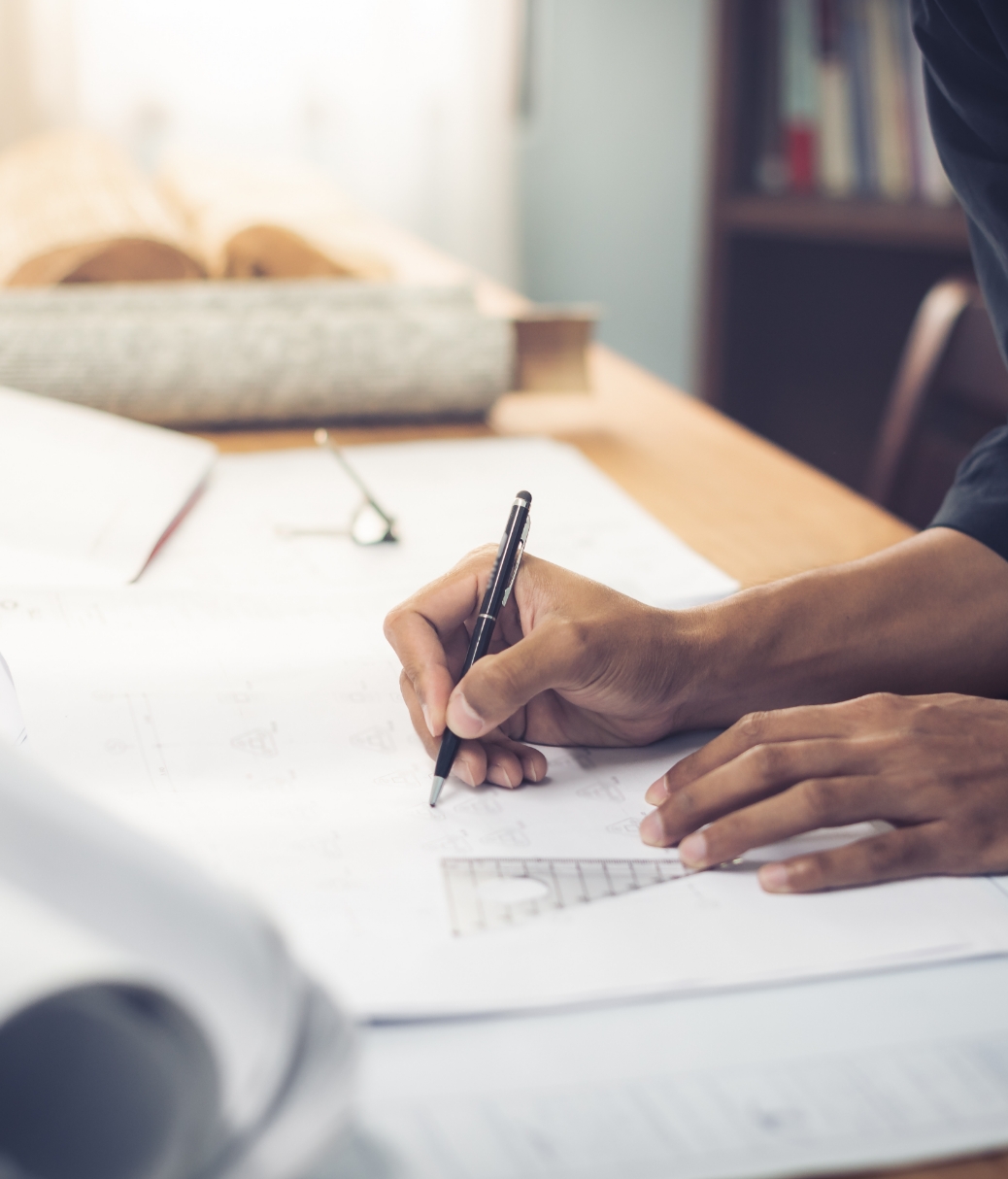 机の上で図面にペンを走らせる人の手元