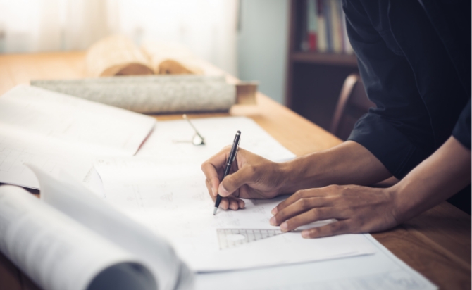 机の上で図面にペンを走らせる人の手元